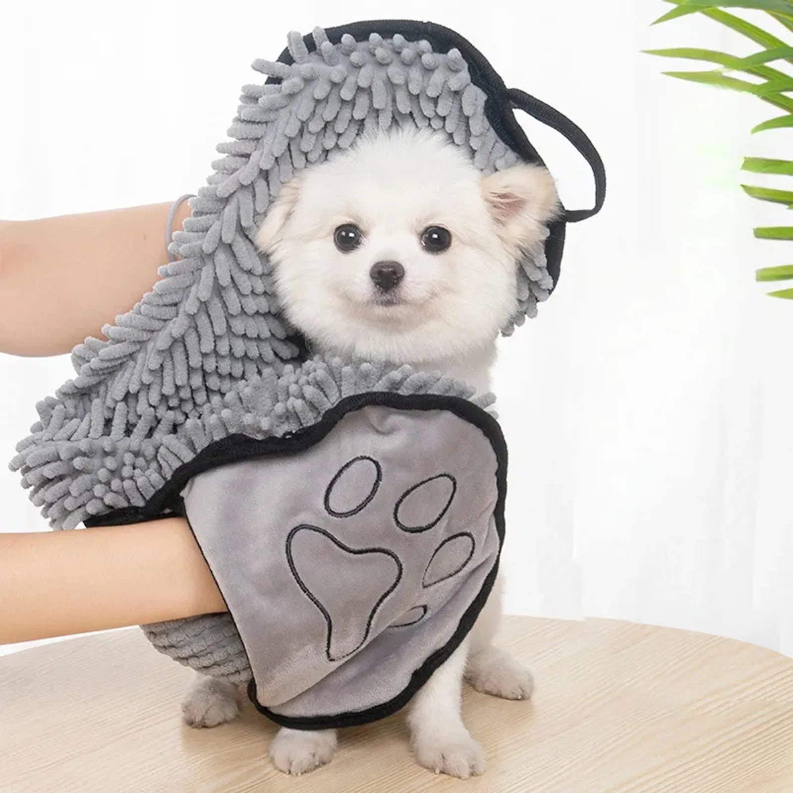 Small white dog being dried with a grey microfiber towel with hand pockets